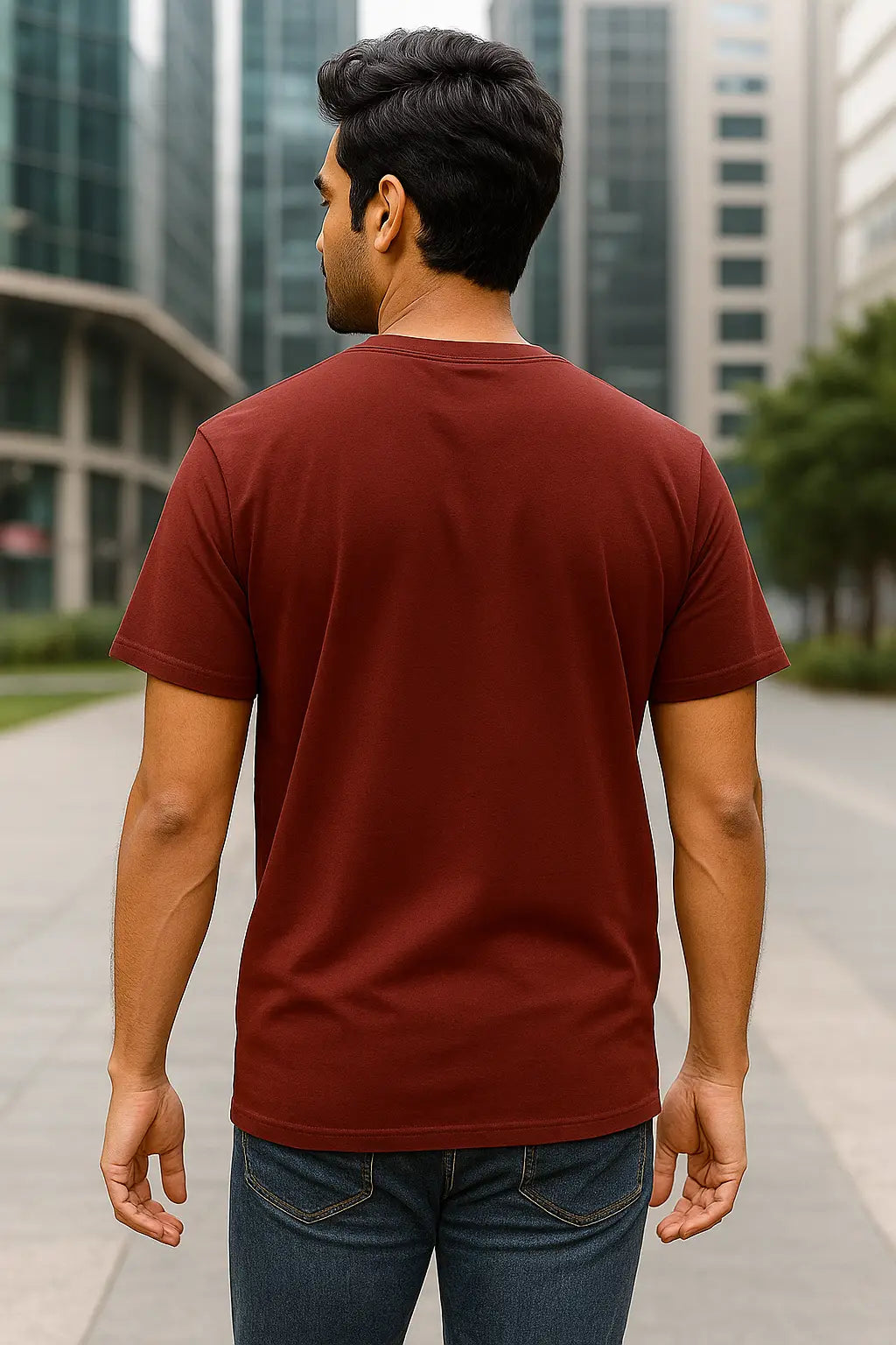 Man wearing a maroon t-shirt and blue jeans walking in an urban setting