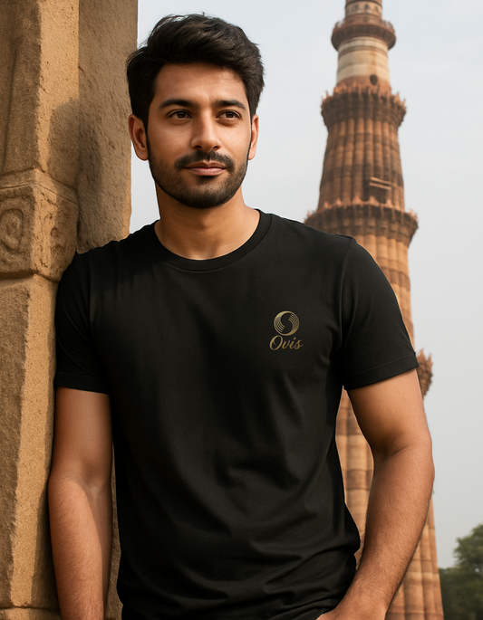 Man wearing a black t-shirt with a logo, standing in front of a historical tower.